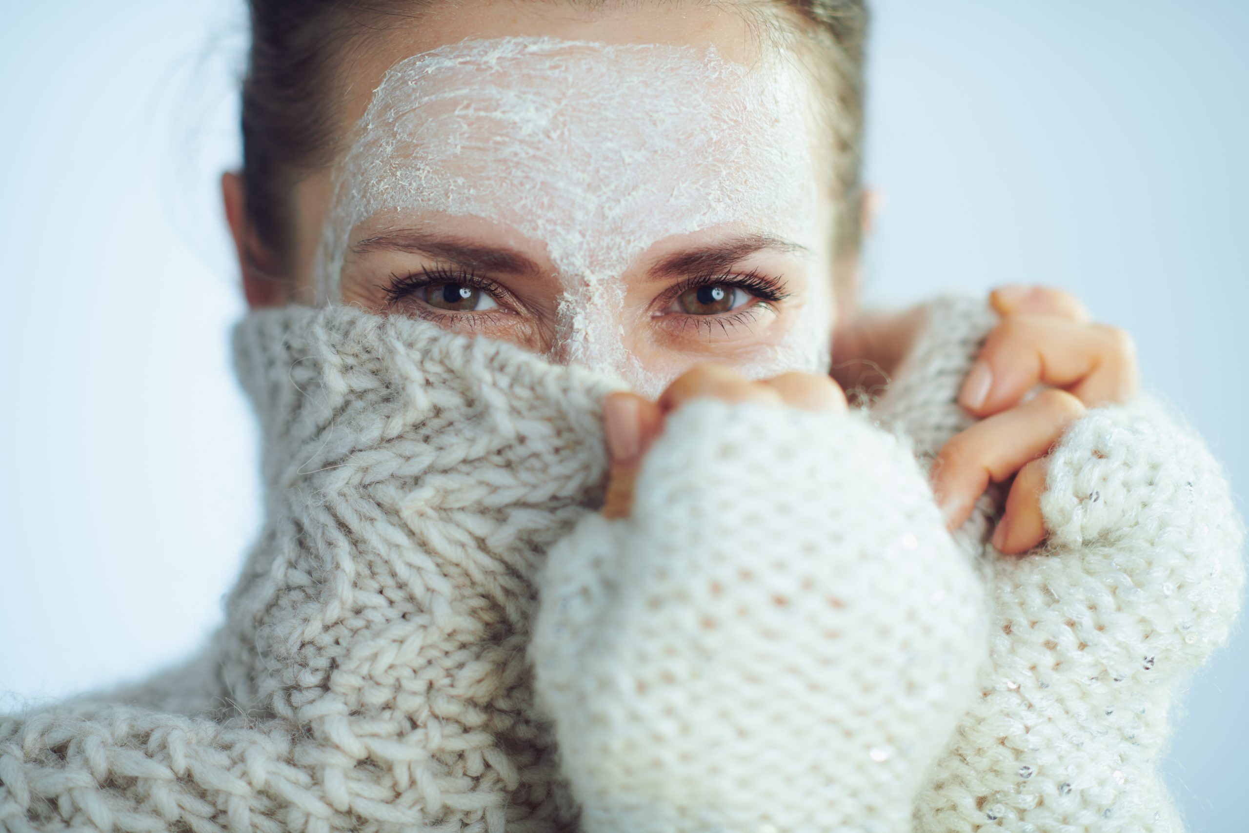 elegant woman with white facial mask hiding behind clothes