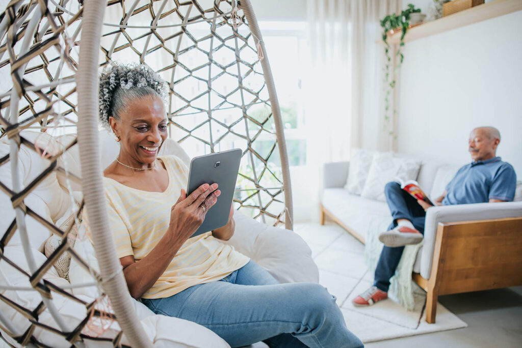 Senior couple in living room, man reading book and woman using digital tablet