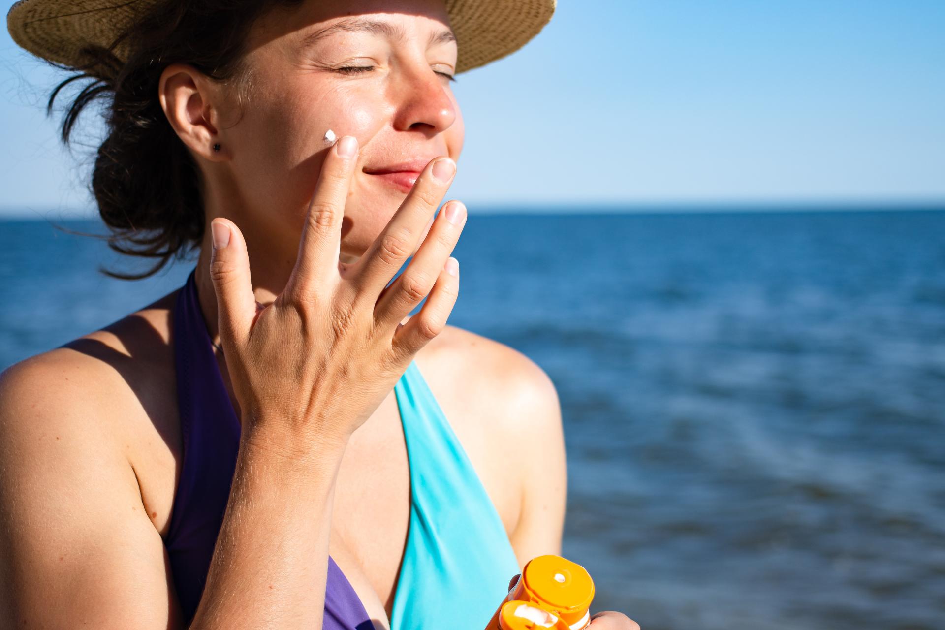 woman in the sun applying sunscreen to face