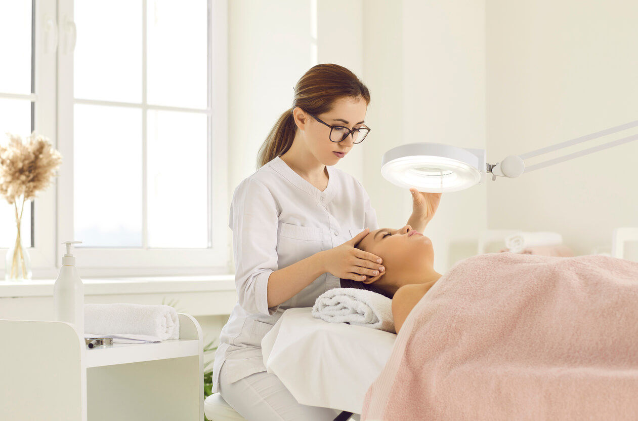 Esthetician examining a client’s skin under a magnifying lamp