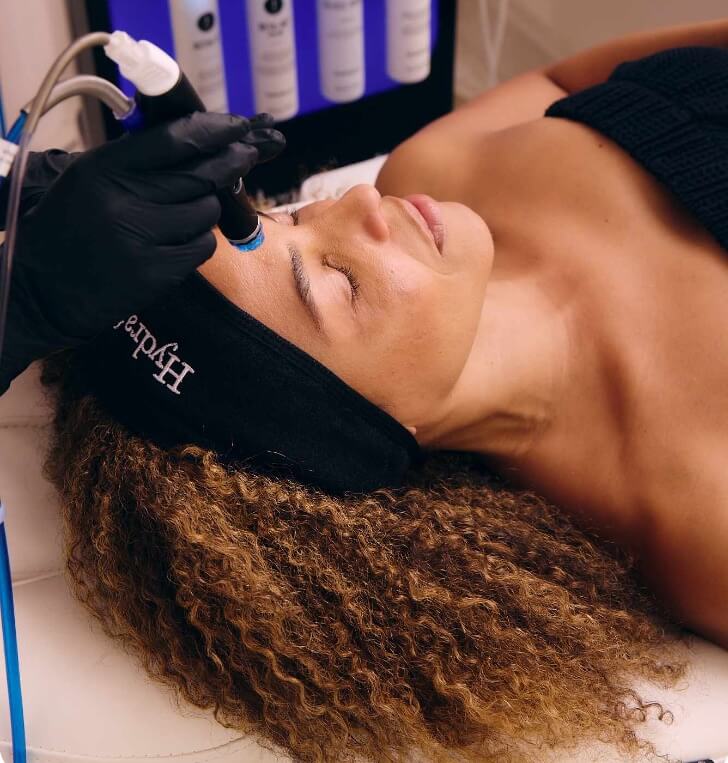 Client relaxing with eyes closed during a HydraFacial treatment as an esthetician glides the HydraFacial wand across the forehead