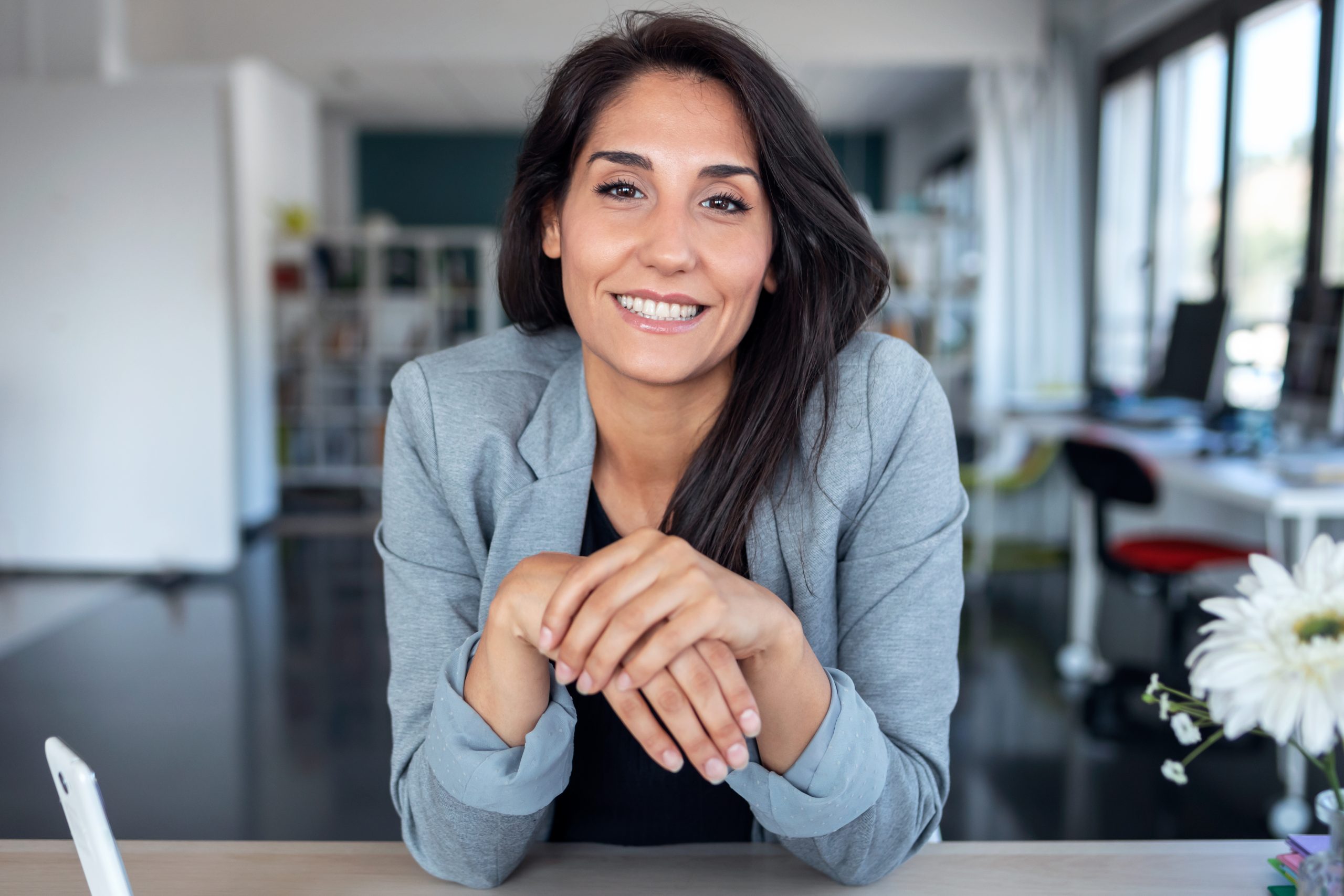Smiling woman in a blazer seated at a desk in a bright office